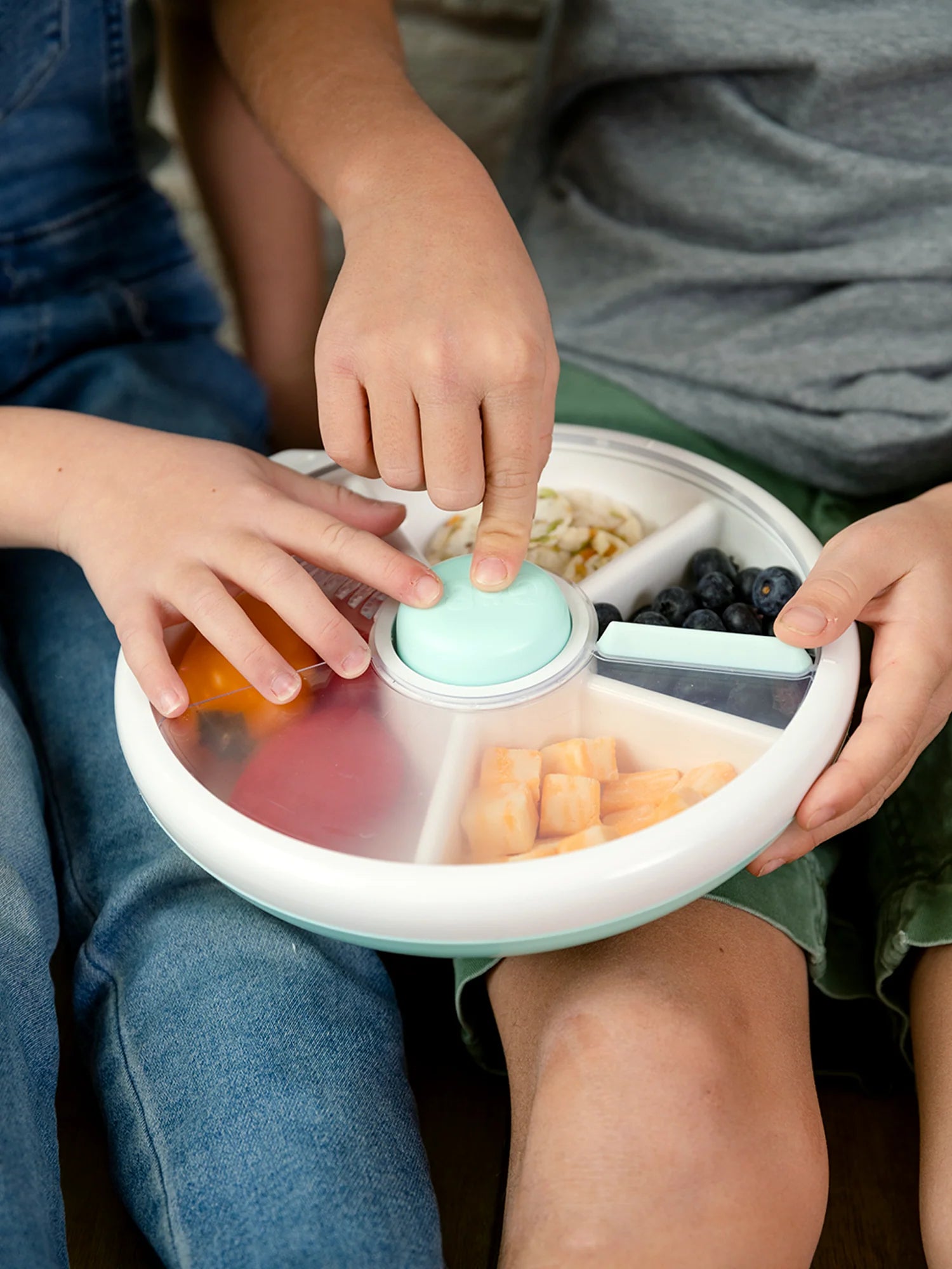 Two kids using a blue GoBe Snack Spinner lunchbox, selecting snacks from different compartments.