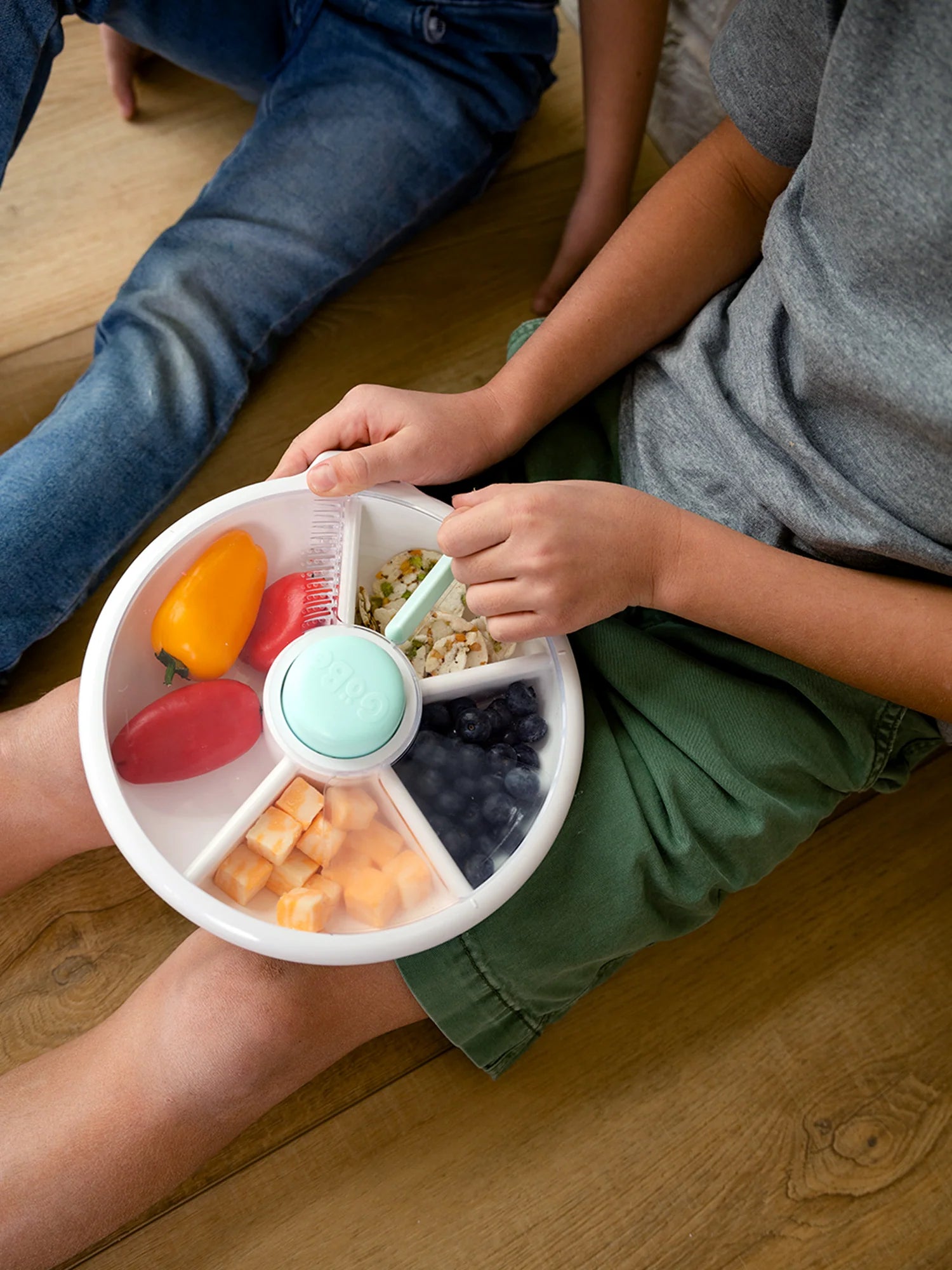 Child holding a GoBe Snack Spinner lunchbox filled with fruits and vegetables, perfect for healthy snacks.