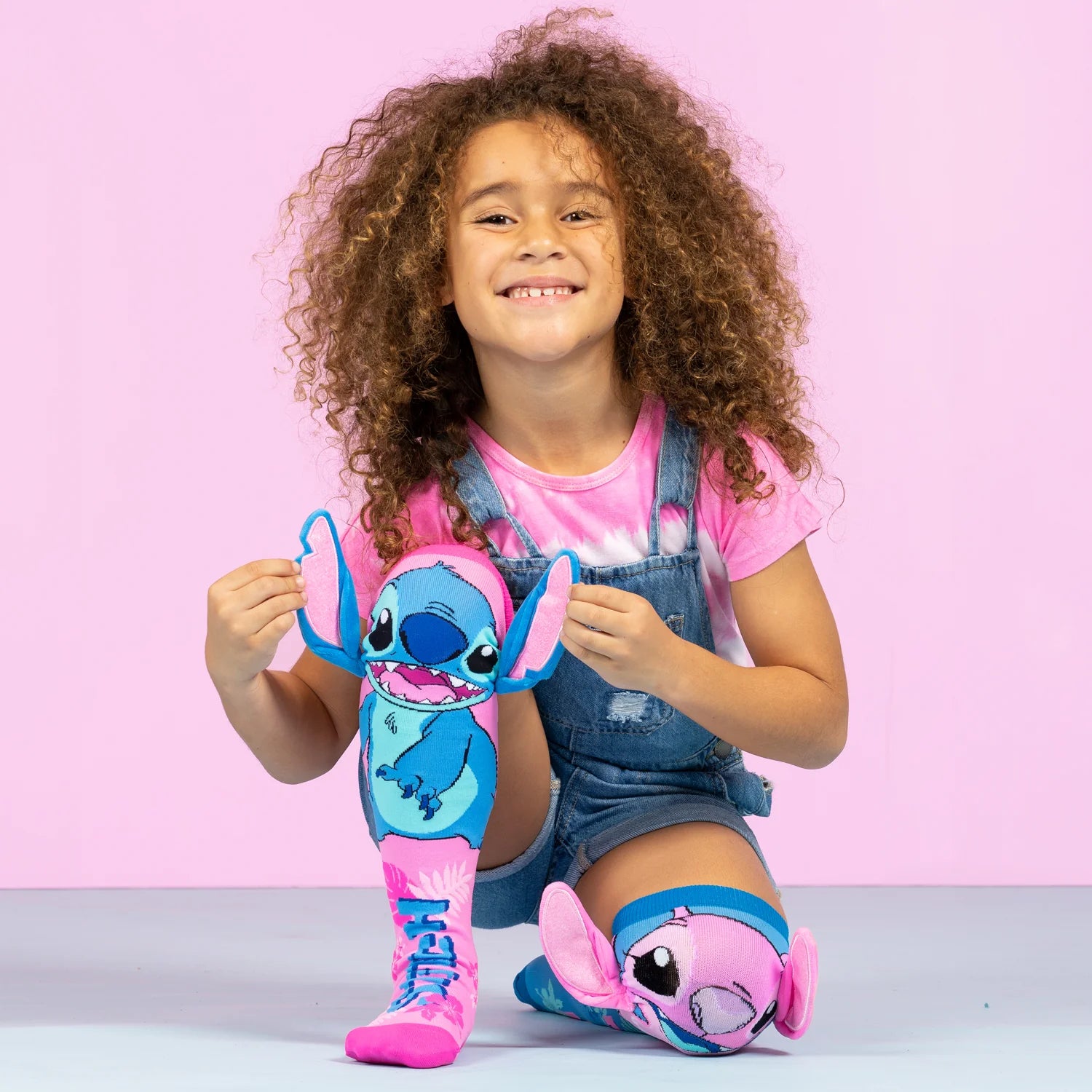 Girl wearing colorful Madmia Stitch socks, playing and smiling against a pink background.