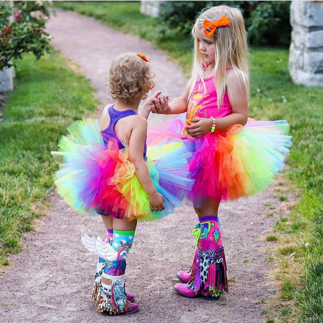 Two young girls wearing colorful tutus and vibrant Madmia socks, enjoying a playful moment outdoors.